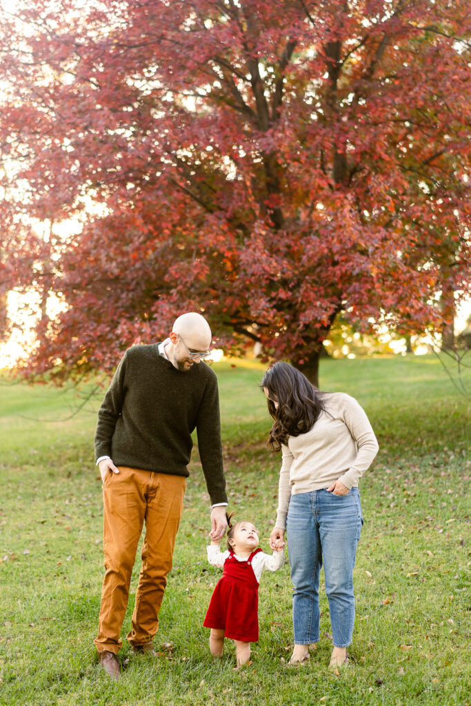 A mom, dad, and toddler holding hands and walking towards the camera. 