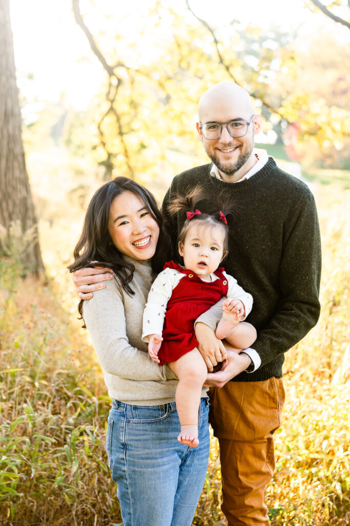 Two adults smiling at the camera while holding a toddler between them.