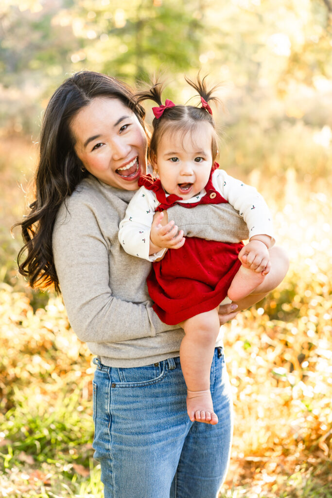 A mom and toddler daughter leaning towards the camera with big smiles on their faces.
