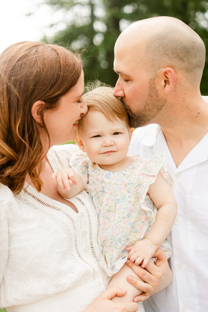 Two parents kissing the head of their baby who is held in between them.