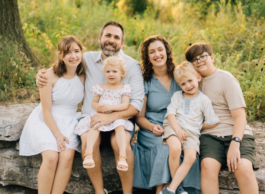 A family sitting on a ledge smiling at the camera at the Forest Park Nature Playscape.
