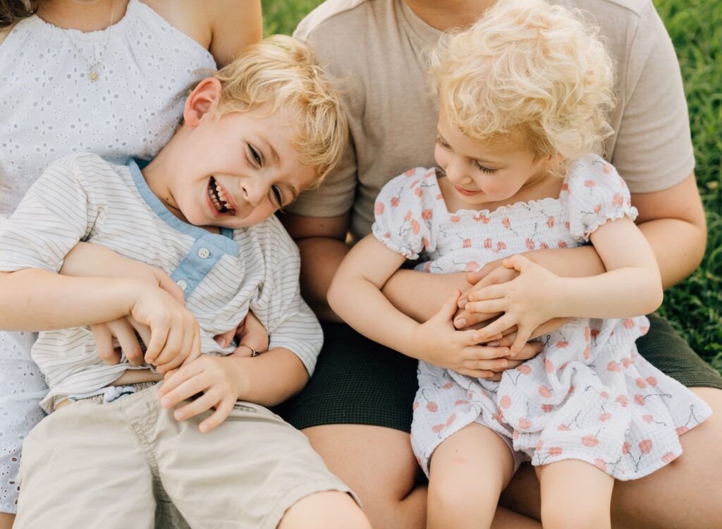Two young kids sitting in their siblings laps and being tickled.