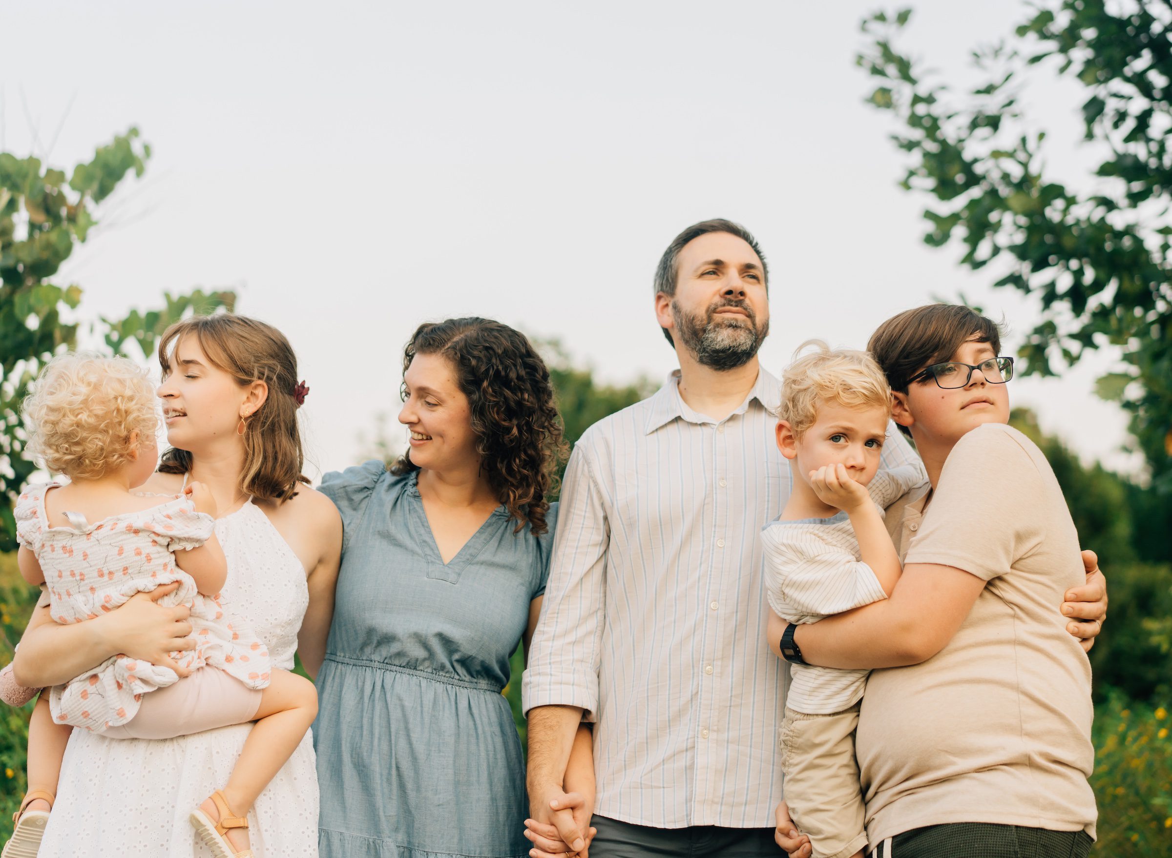 Family looking off in different directions at the Forest Park Nature Playscape. The sky is behind their heads and they are framed by the trees.