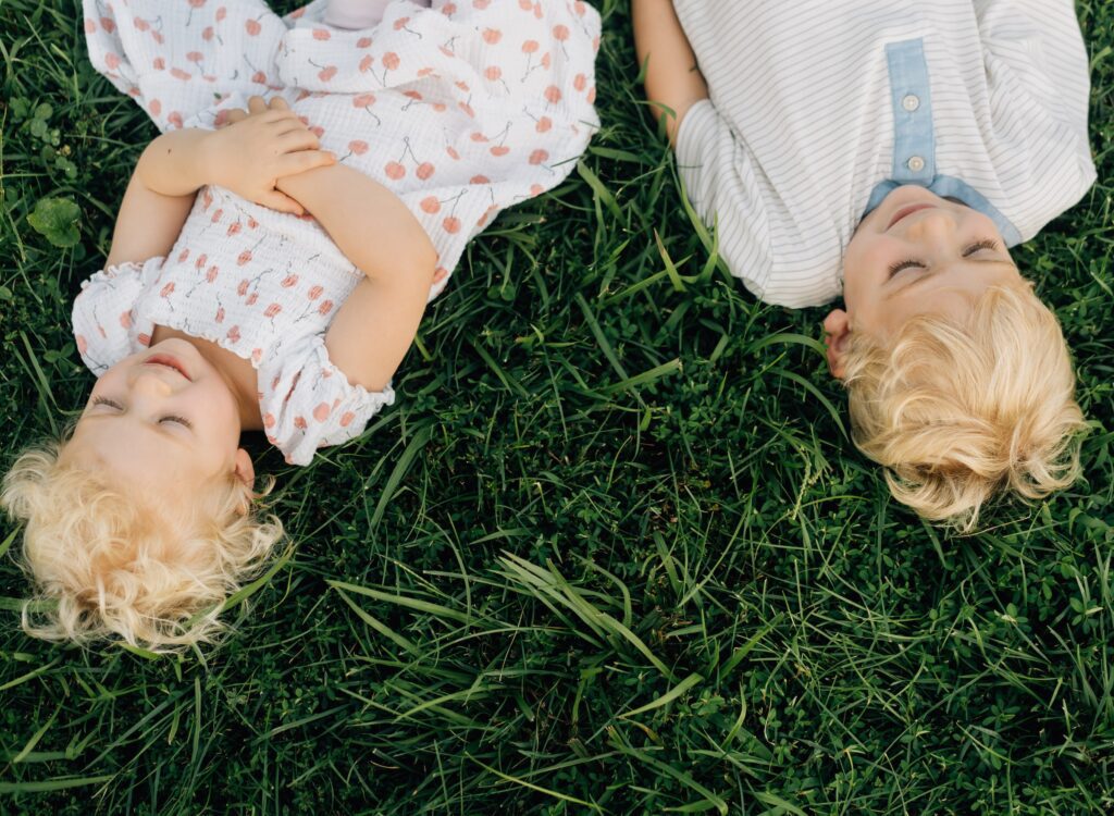 Two blond haired kids laying in the grass and smiling. The image is hot from above.