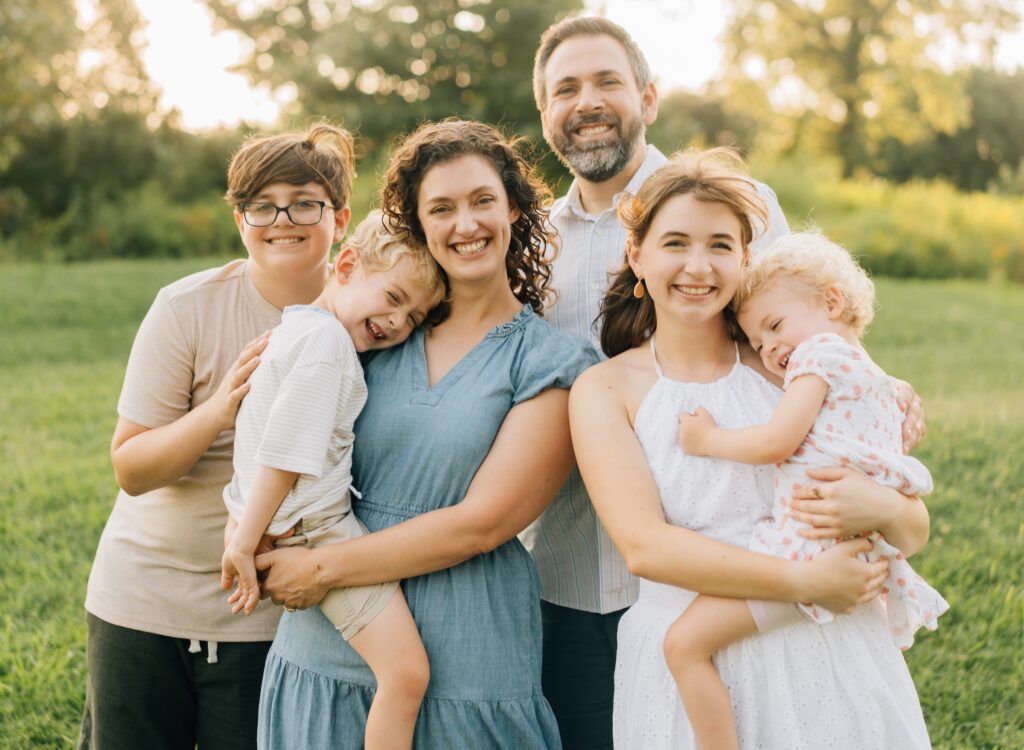 A family standing close together and smiling at the camera for Forest Park Nature Playscape family photos.