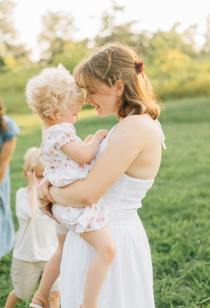A teen girl holds a toddler girl and touches her nose to the toddler's forehead.
