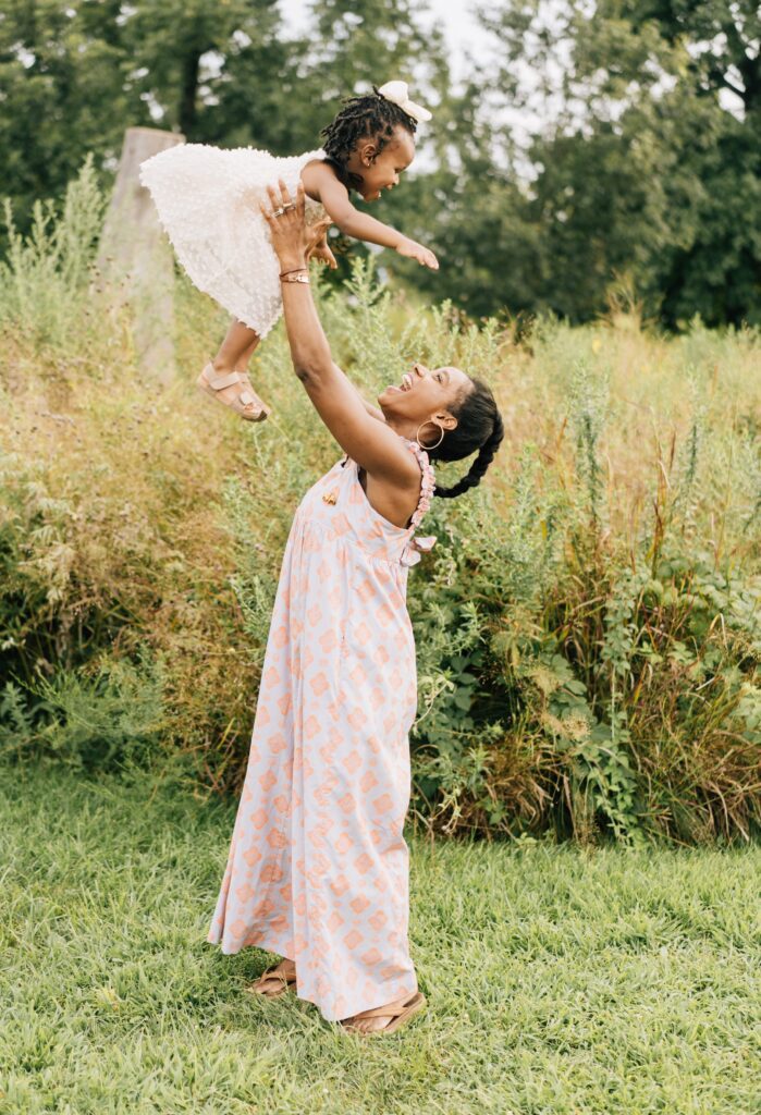 A mom faces their daughter and lift her up into the air. She has a big smile on her face.