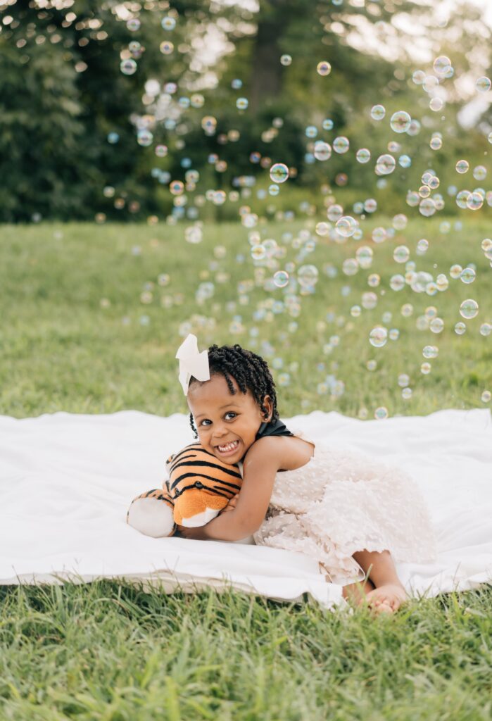 A little girls hugs her tiger stuffy with bubbles in the background.
