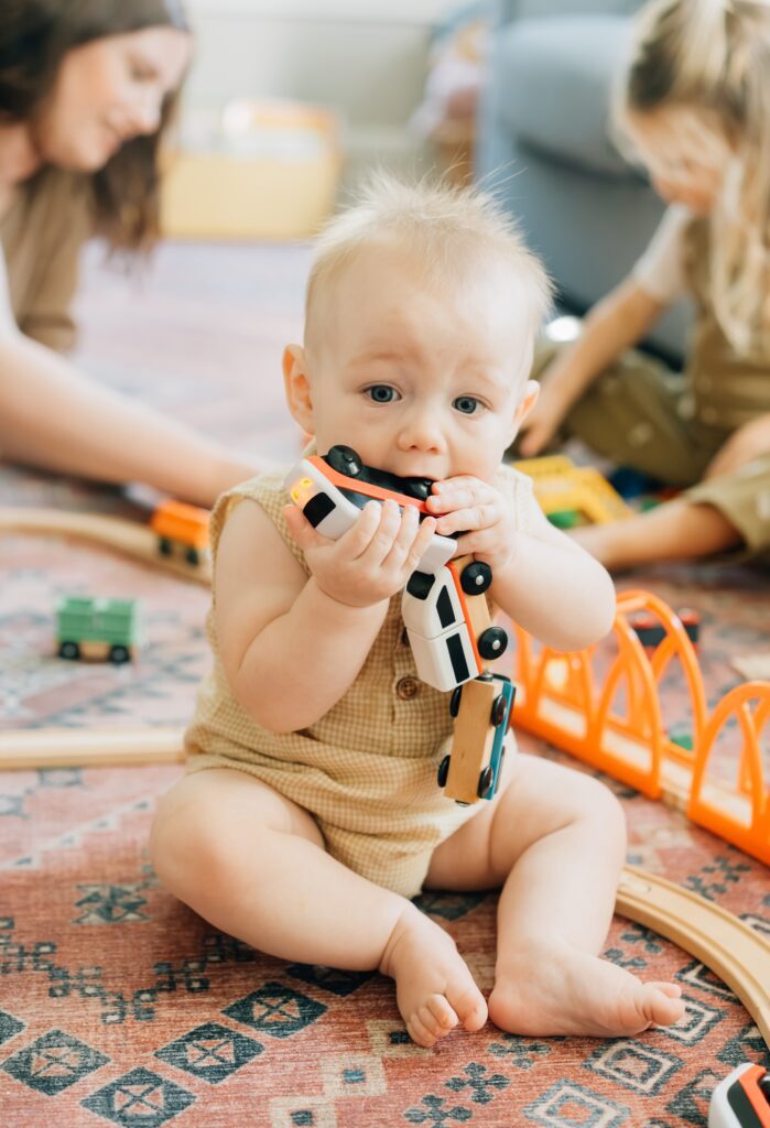 A baby gnawing on a toy wooden train.