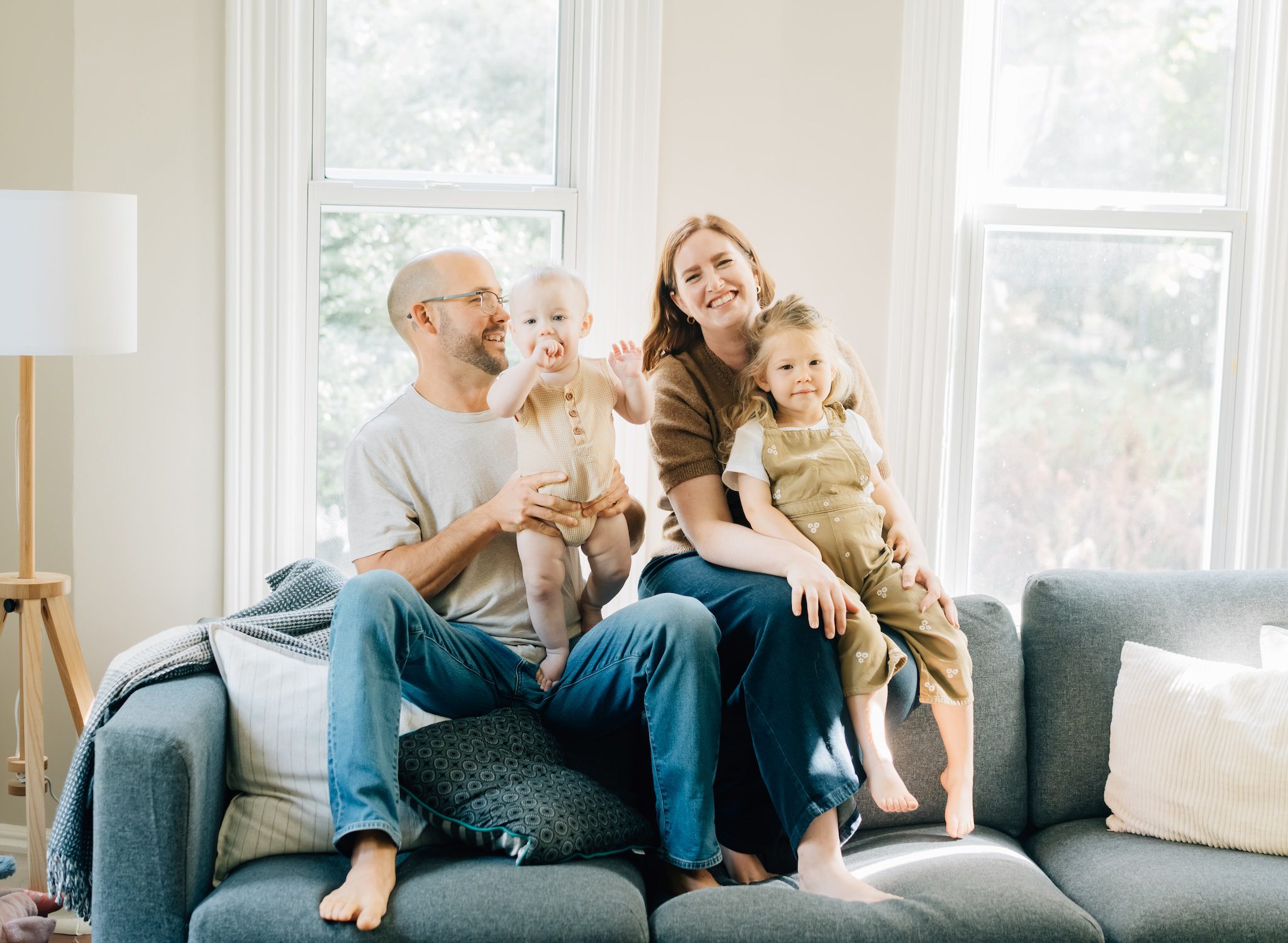 A family sits on the top of their couch smiling at each other for their St. Louis In home family photos