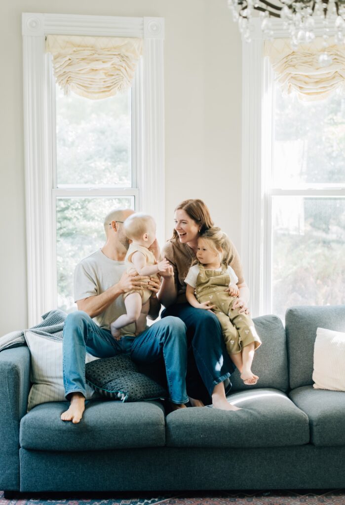 A family sits on the top of their couch smiling at each other for their St. Louis In home family photos