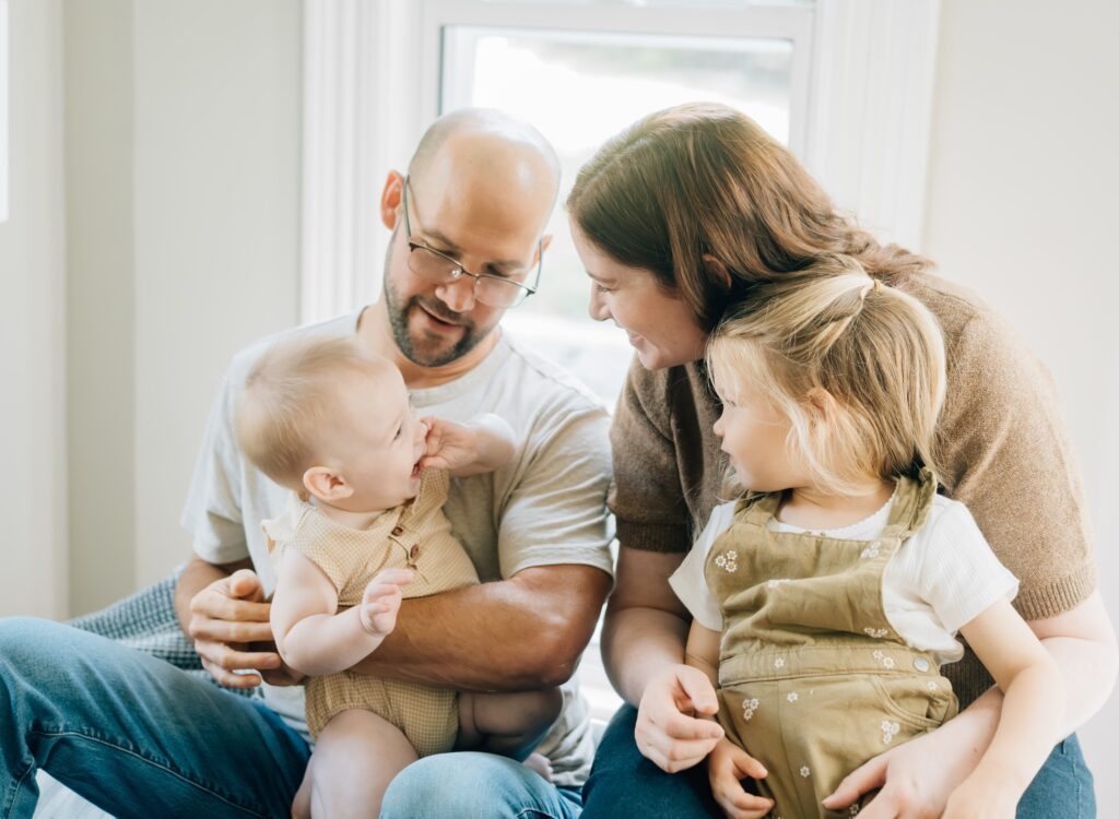 A family sitting at the top of their couch and smiling at each other.