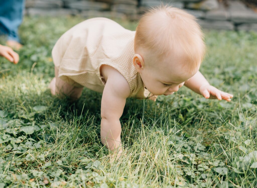 A baby crawls in the grass.