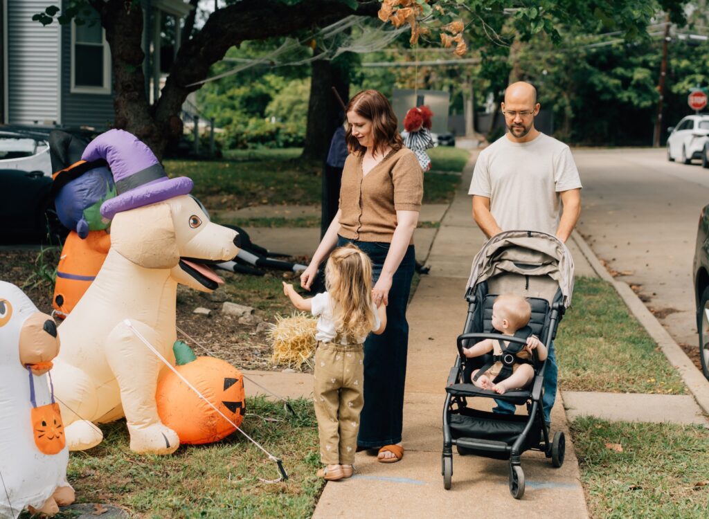 A family looking at Halloween decorations in their neighborhood while they are on a walk.