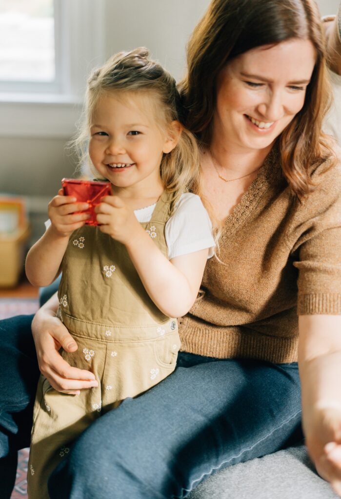 A girl smiling at the camera while holding a red magnatile for her St. Louis family in home photos.