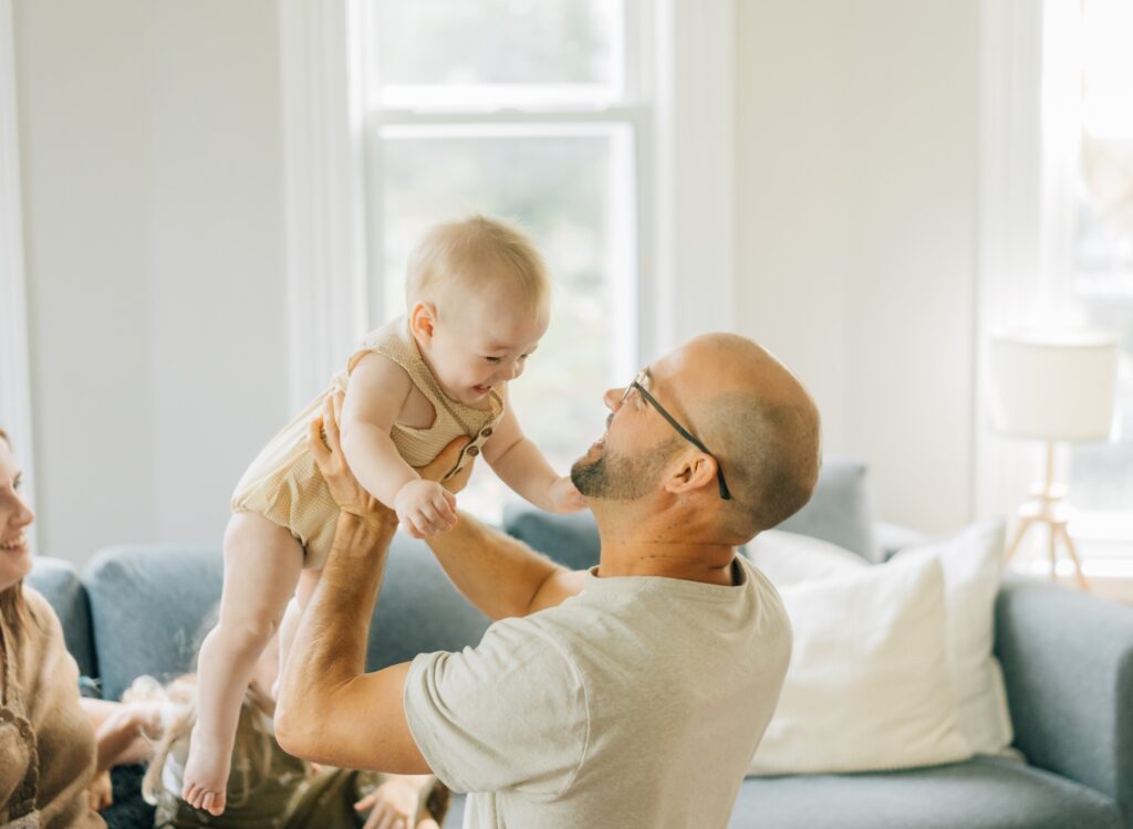 A father raising his baby up into the air while the baby is smiling.